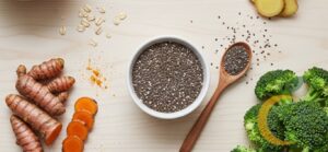 Cinco alimentos funcionais dispostos em uma composição bonita e colorida sobre uma mesa clara: cúrcuma, gengibre, brócolis, aveia em flocos e sementes de chia. Estética clean, luz natural e sensação de saúde vibrante.